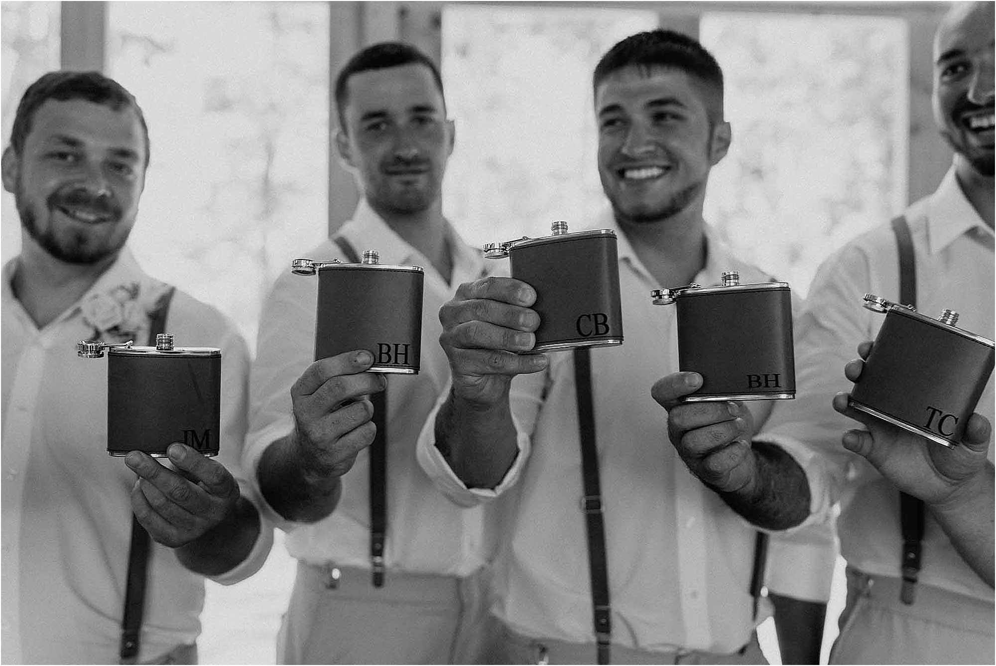 groom and groomsmen holding up personalized flasks