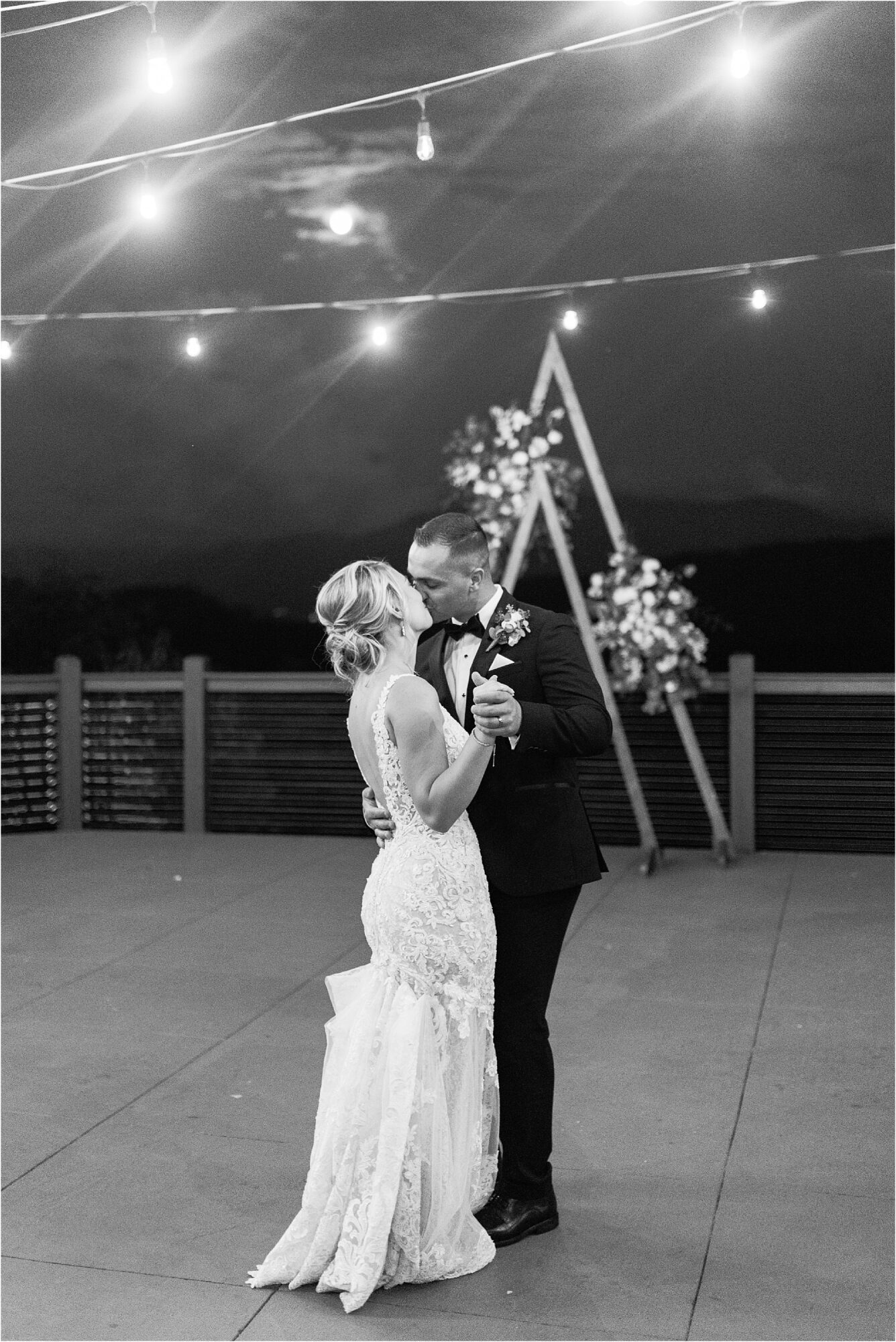 black and white photo of bride and groom dancing under twinkle lights