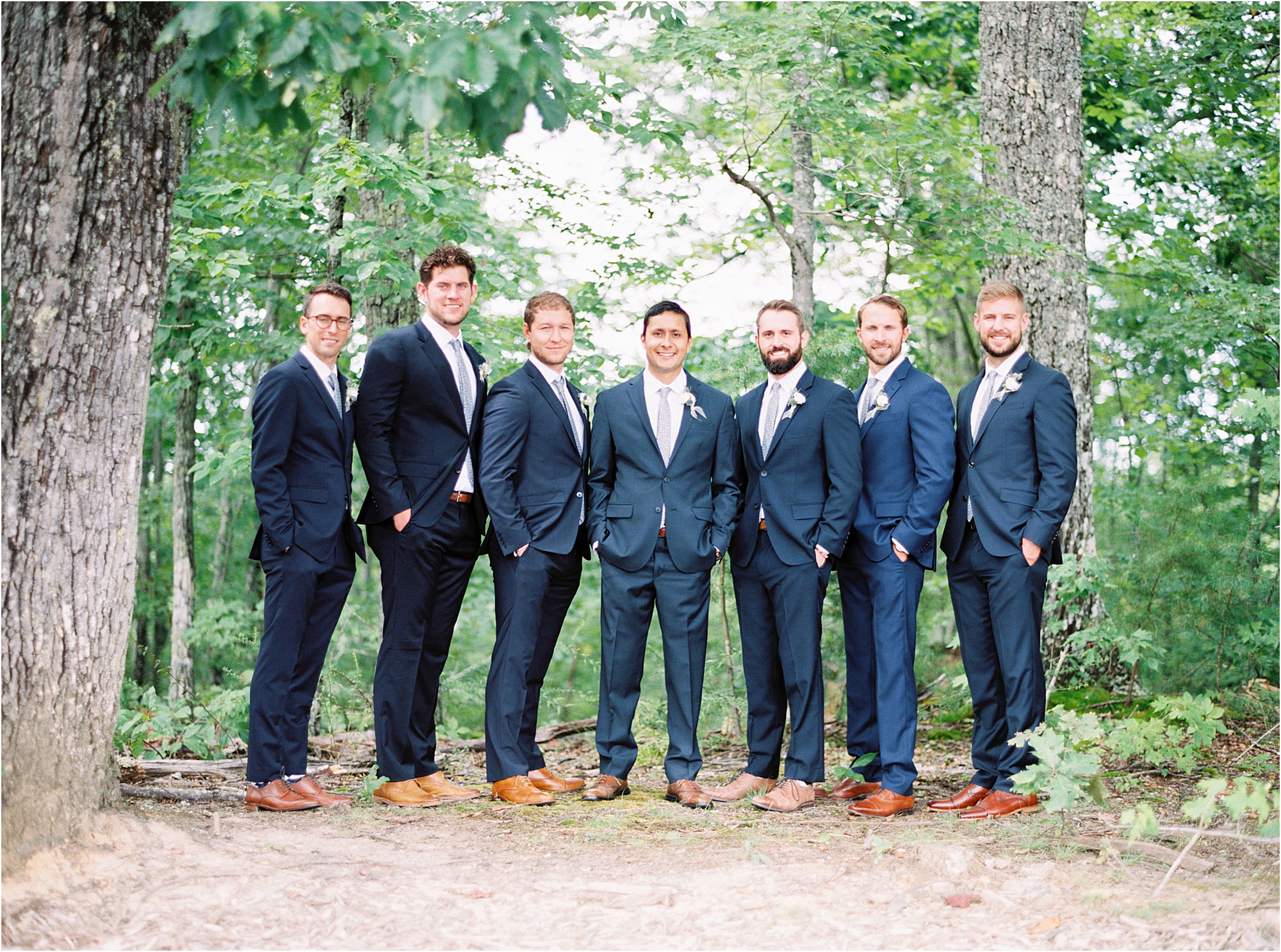 groom and groomsmen in blue suits standing in the woods
