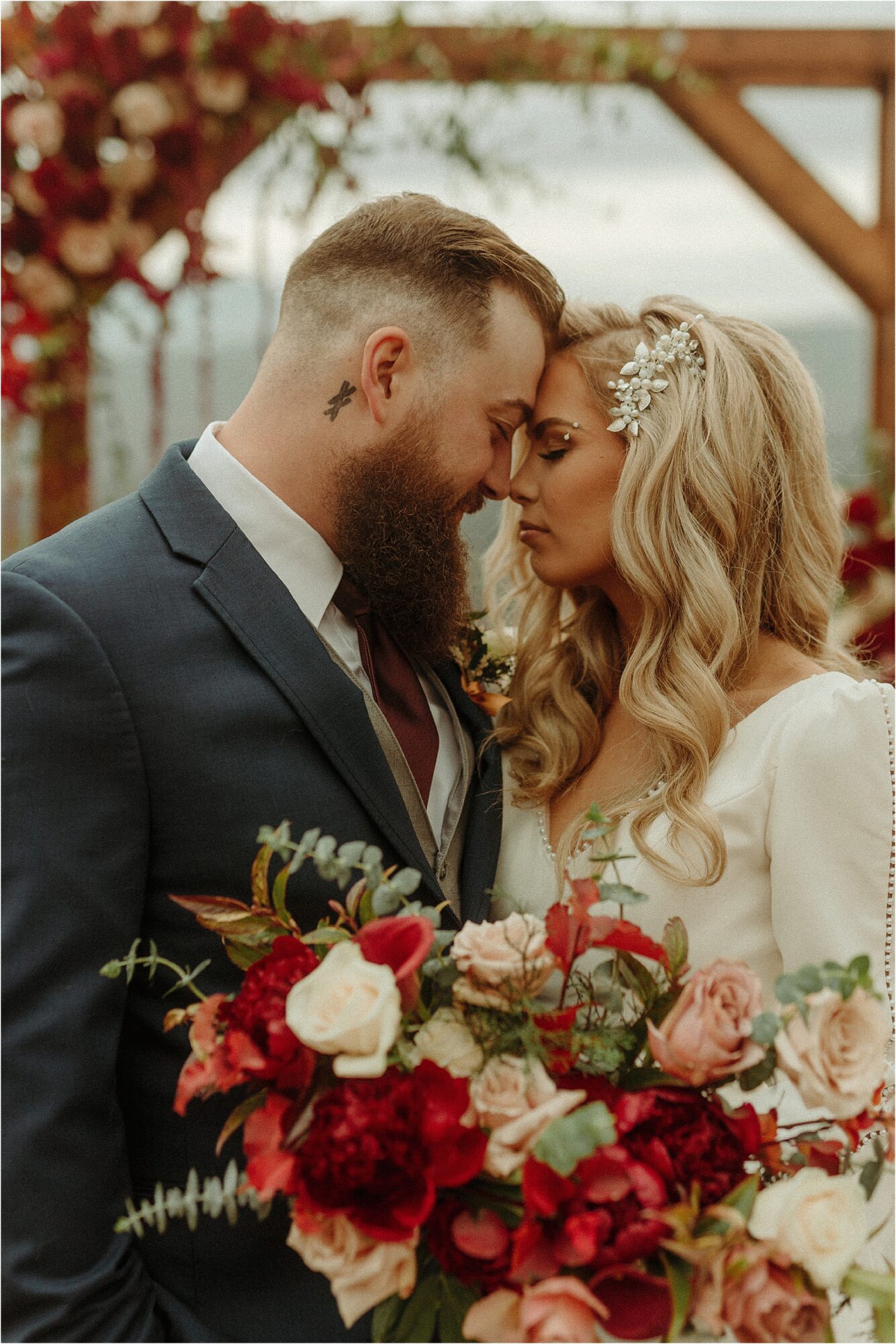 man and woman touch foreheads together while holding large jewel tone bouquet