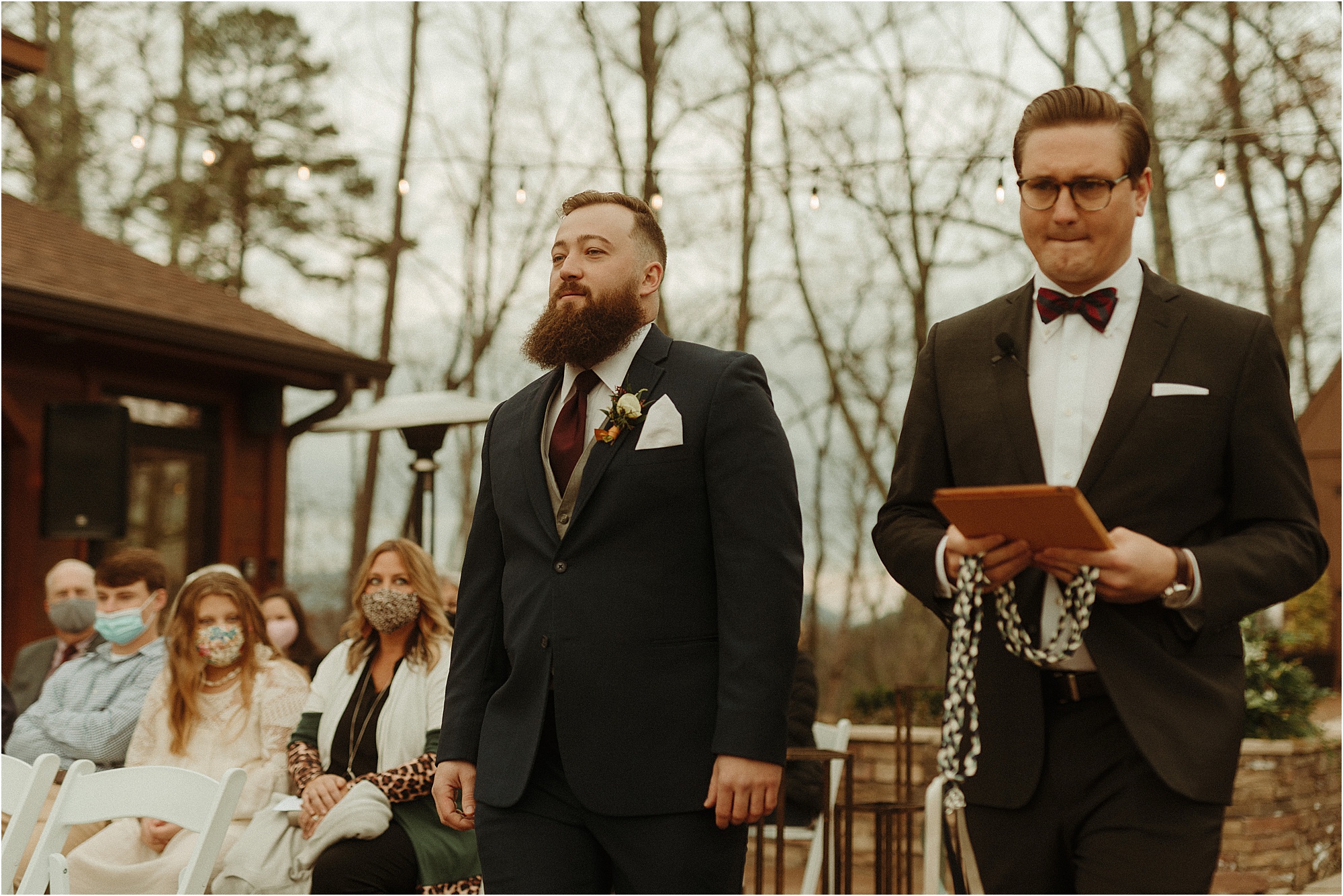 groom in blue suit and burgundy tie walks down wedding aisle