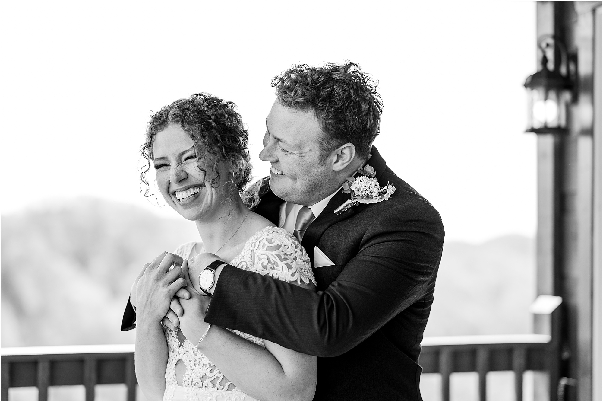 groom hugs bride from behind on cabin porch