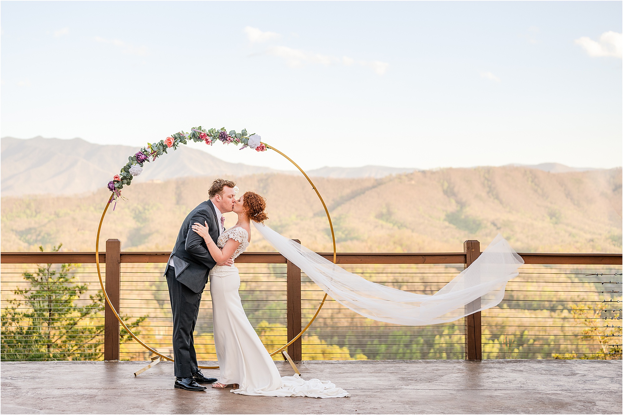 groom dips bride infront of circle wedding arbor with veil blowing in the wind