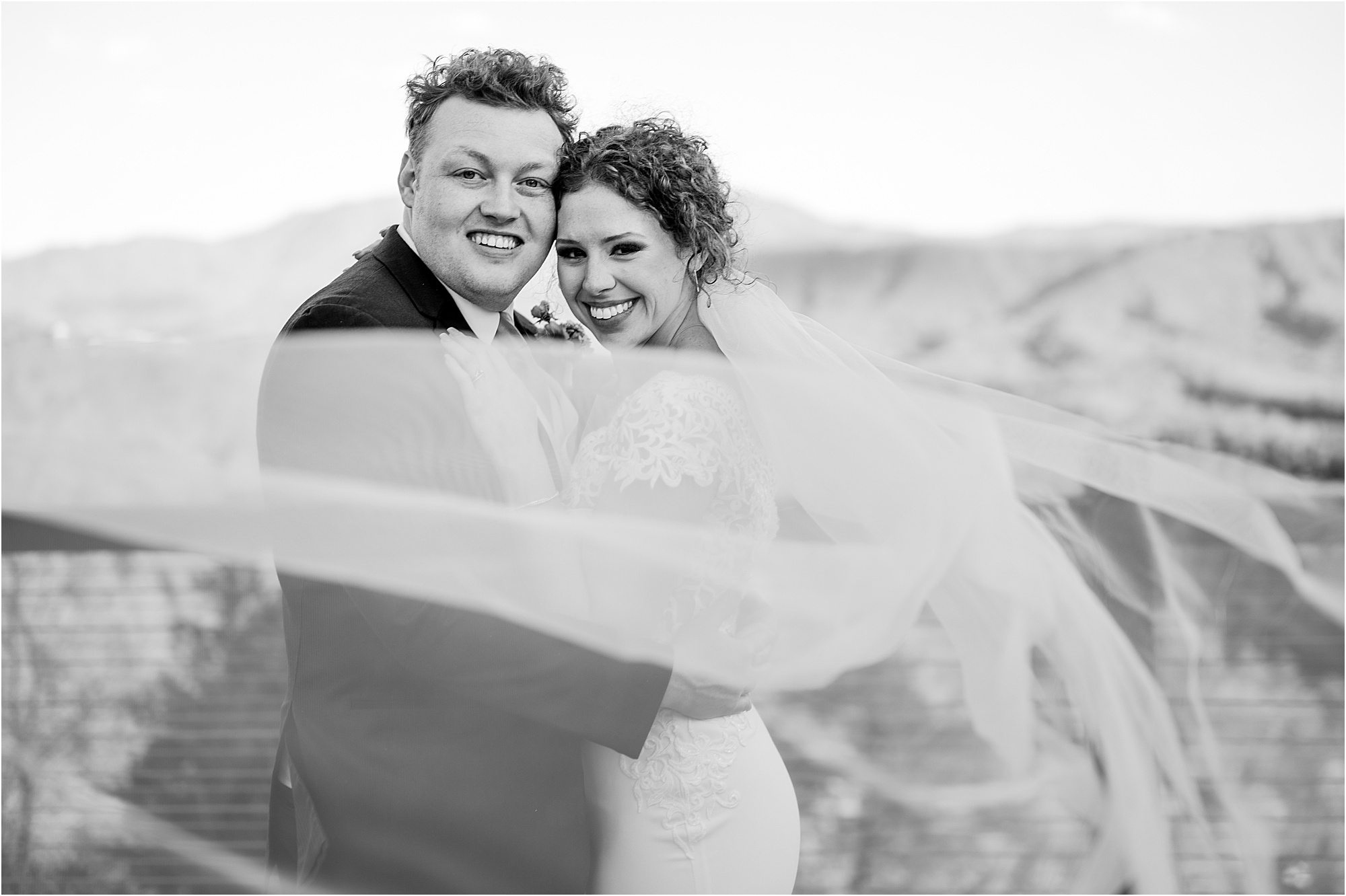 black and white portrait of bride and groom with veil blowing in the wind